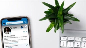 a phone with linkedin profile for Tim Schmidbauer's profile open next to a plant and Apply keyboard